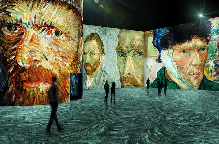 People walking through a giant digital art gallery featuring works from Van Gogh.