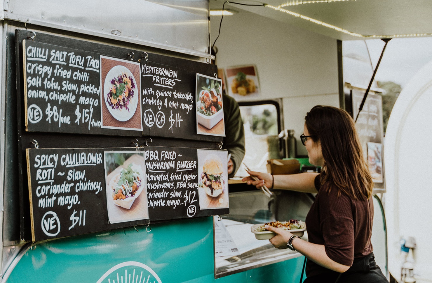 A girl stands at the window of a food truck at the vegan food festival.