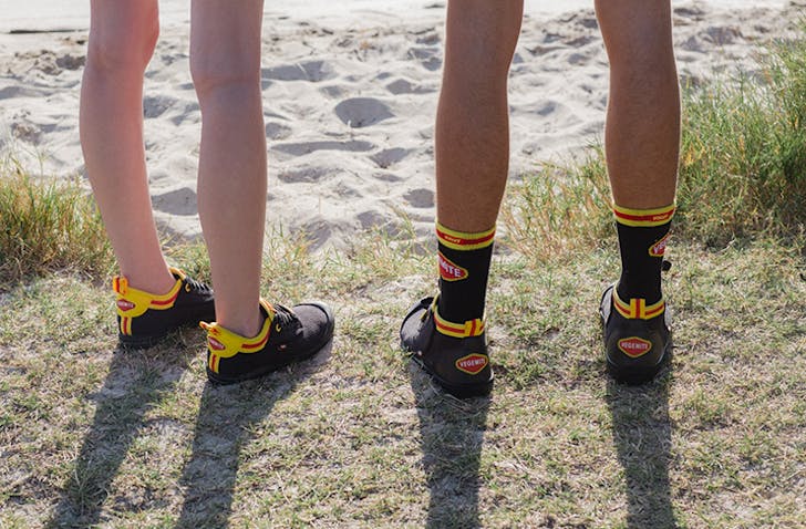 Two people standing by the beach wearing Vegemite branded sneakers.