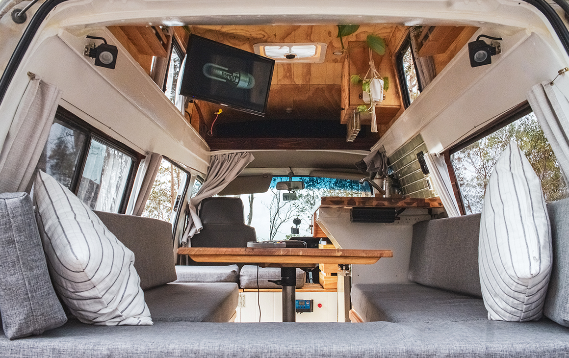 Inside of a vintage campervan with a tv, small table and kitchen