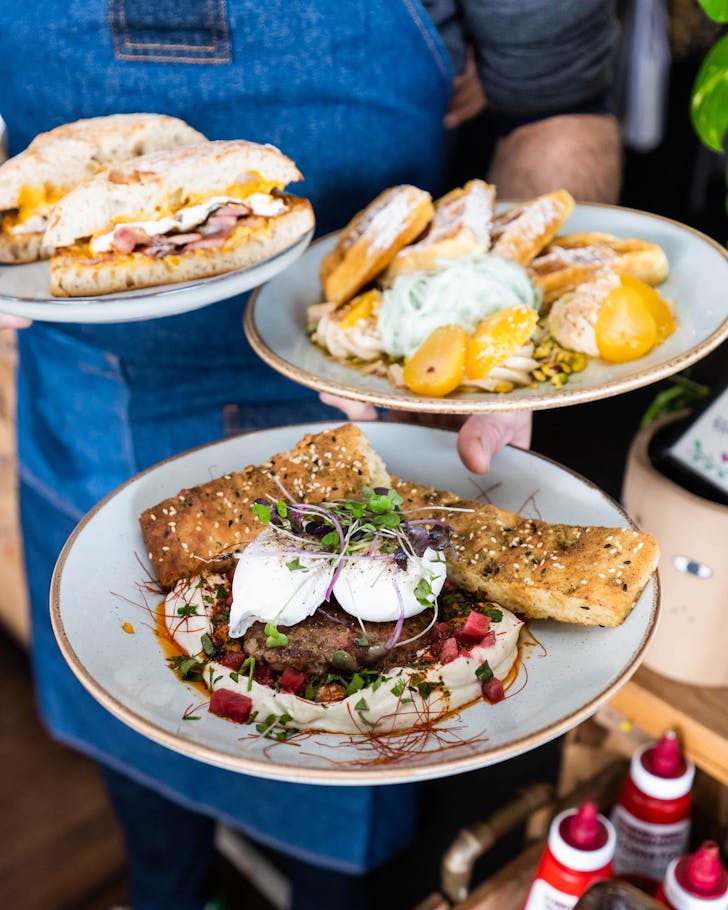 A waiter carries three breakfast dishes at Social Manna in Victoria Park