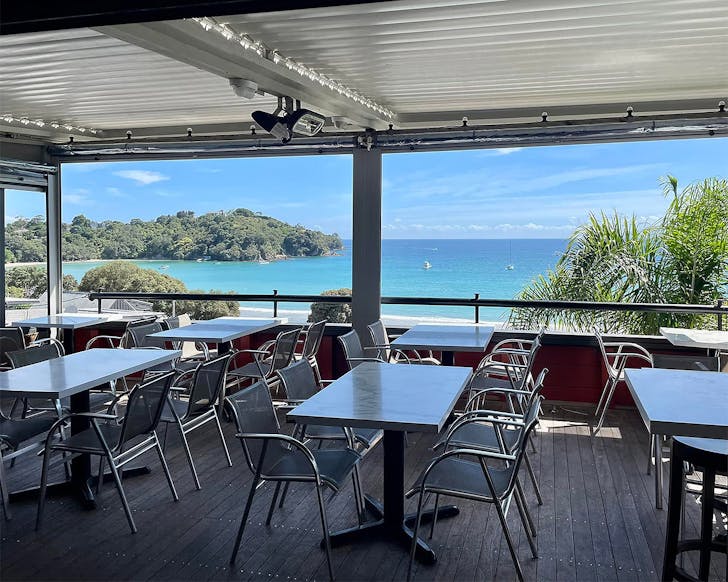 Tables and chairs look out over a stunning view of Oneroa beach at Vino Vino.