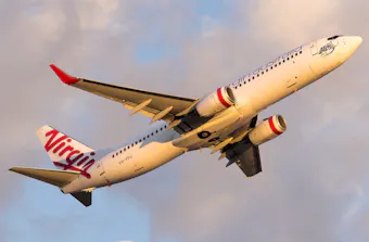 Close up of a Virgin Australia plane flying against a cloudy sky.