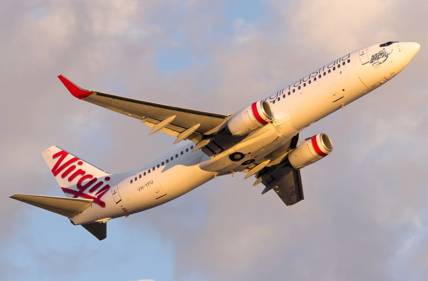 Close up of a Virgin Australia plane flying against a cloudy sky.