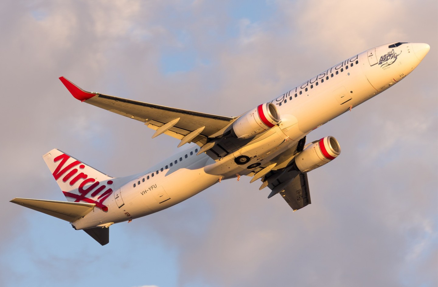 Close up of a Virgin Australia plane flying against a cloudy sky.