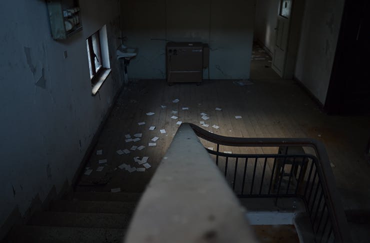 The interior of a spooky, derelict house. Paper is scattered across the old wooden floorboards.