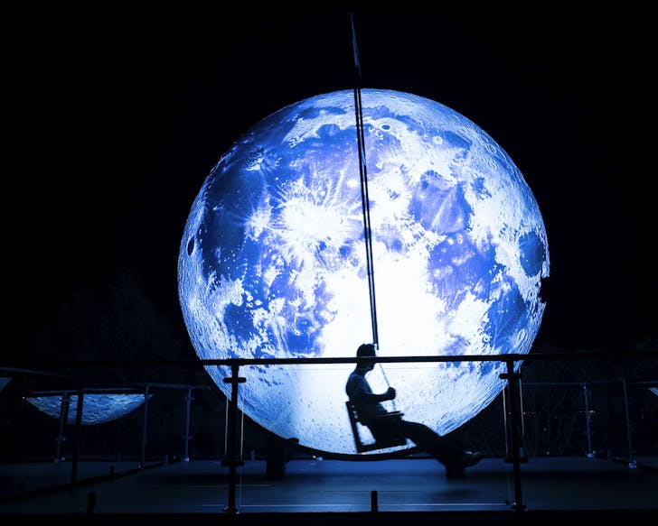 a person swings in front of a large glowing moon at vivid sydney 2025