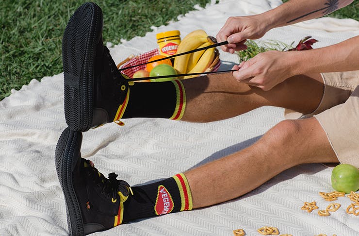 A pair of Vegemite-branded Volleys sneakers on a white picnic rug.