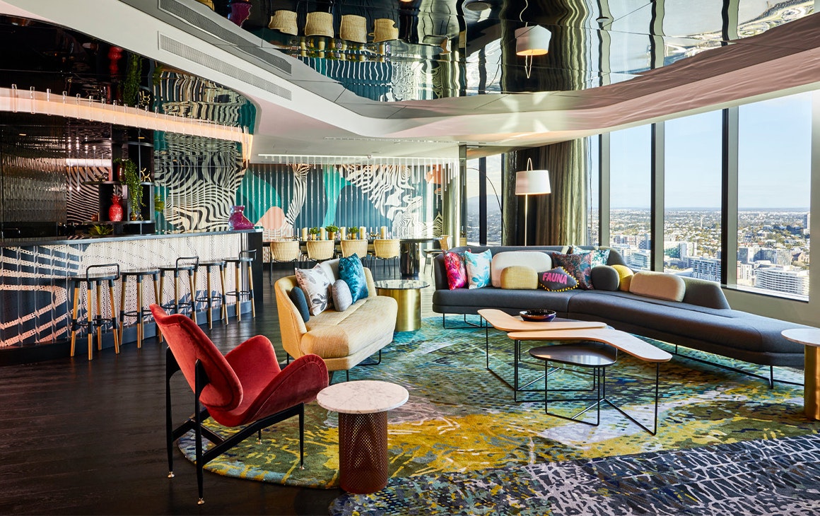 Interior of W Brisbane's Wow Suite, with floor to ceiling windows overlooking the river and luxe furnishings.