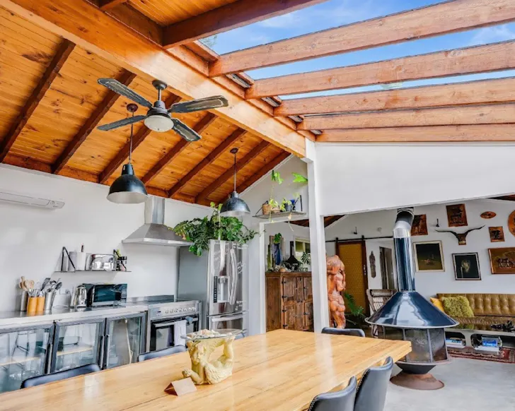 Open-plan coastal living space with timber ceilings, skylights, a fireplace, vintage decor and dining area.