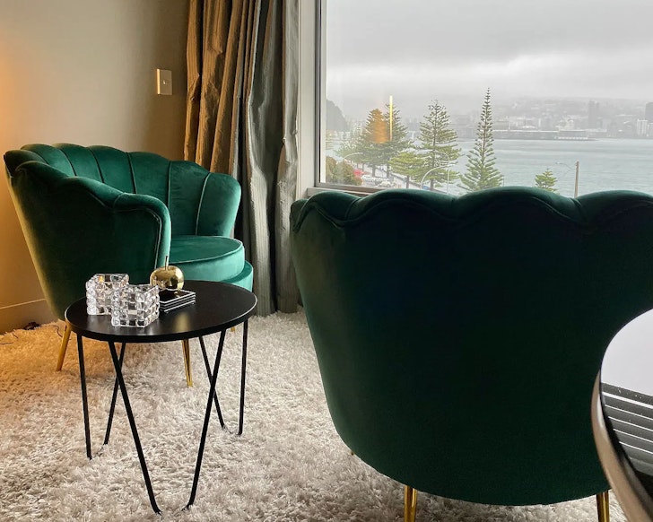 Green velvet chairs look out over the water at Absolute Waterfront Oriental Bay one of the best Wellington Airbnbs