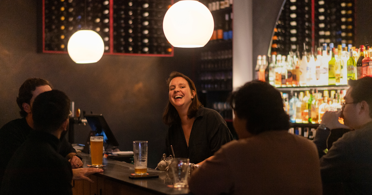 the co-owner alli laughing behind bar with regulars at We Three Bar in marrickville sydney