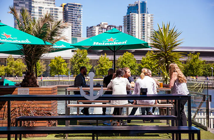 People dining at a pub by the docks of the Yarra River on a sunny day.