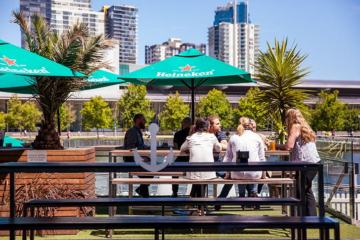 People dining at a pub by the docks of the Yarra River on a sunny day.