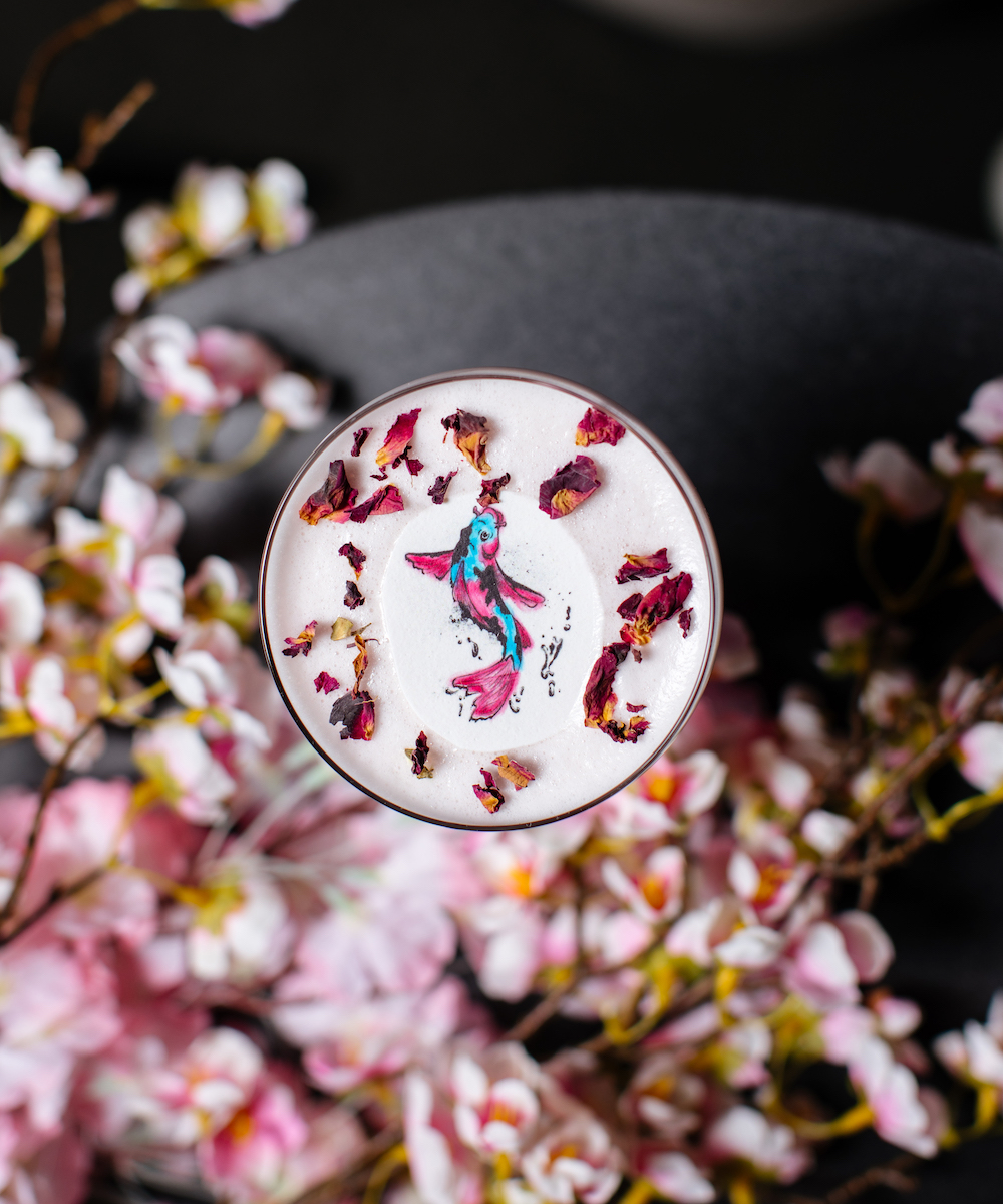 Looking down at a cocktail which has a koi fish and cherry blossom design on the top