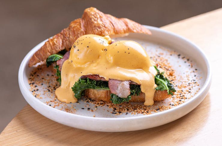 a croissant topped with a poached egg and hollandaise sauce