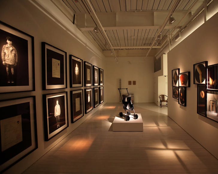 A wide shot inside of the White Rabbit Gallery featuring dim lighting that spotlights on the artworks hanging on the walls.