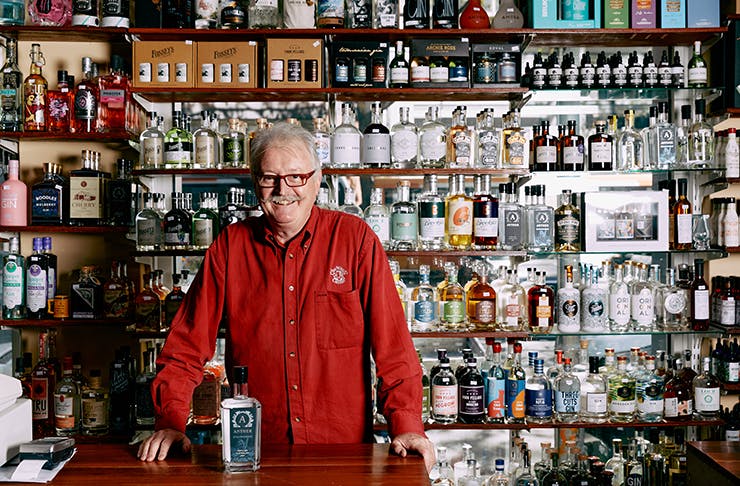 A man in a red shirt standing in front of shelves of alcohol.
