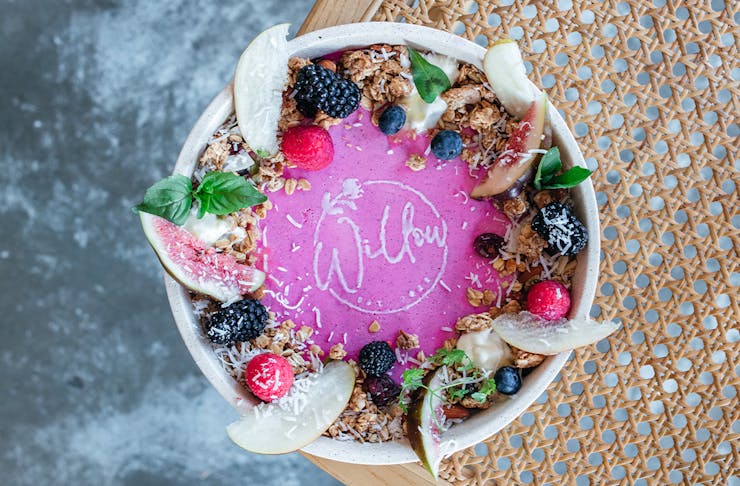 a bowl of pink panna cotta with fruit and granola seen from the top down