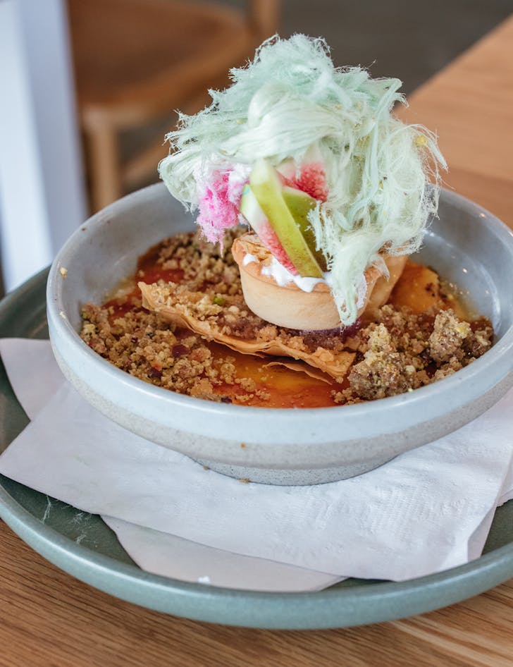 a bowl of brulee topped with a small tart, figs and fairy floss