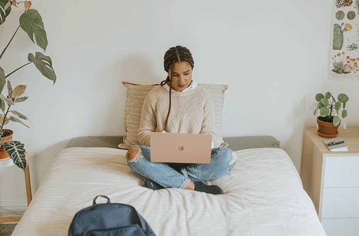 Woman sitting on the bed with her legs crossed working on a laptop computer.