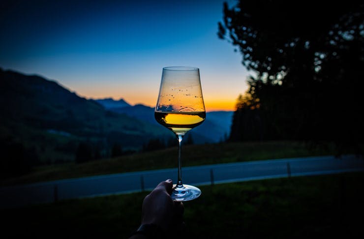 A wine glass, half filled with white wine held up against a sunset. 