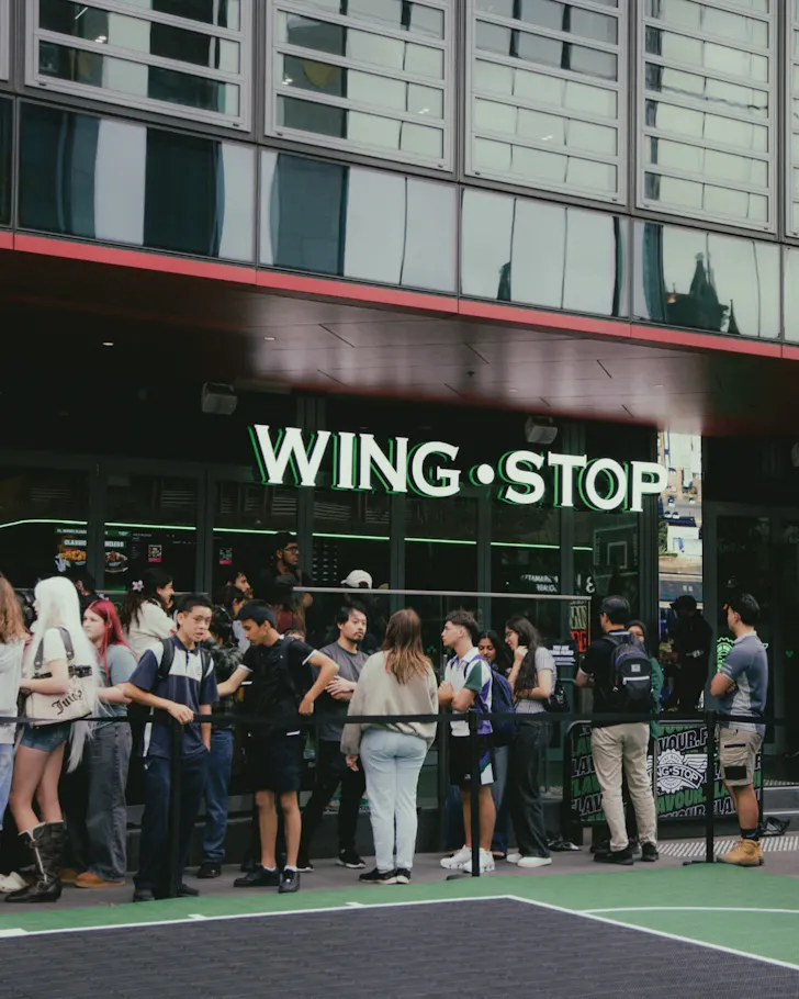People queue outside Wingstop's Kings Cross restaurant in Sydney on opening week, waiting beneath the illuminated storefront sign.