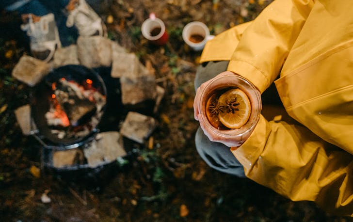 a person holding a mug of mulled wine by a fire
