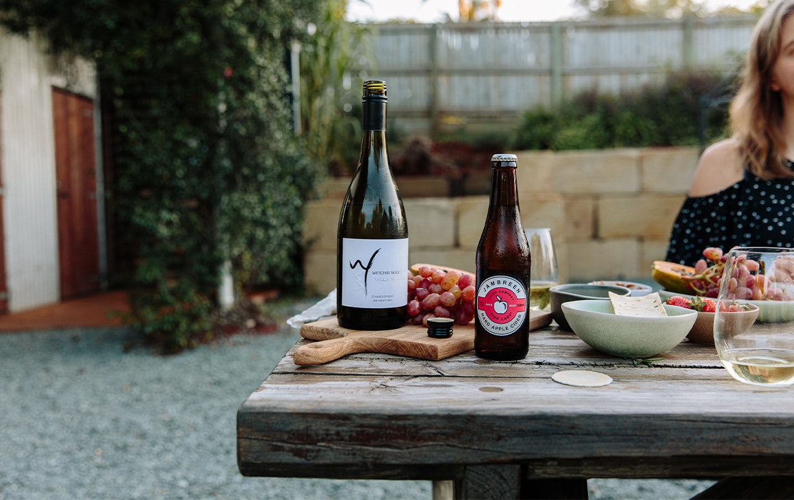 A bottle of wine and cider on a table with plates and boards