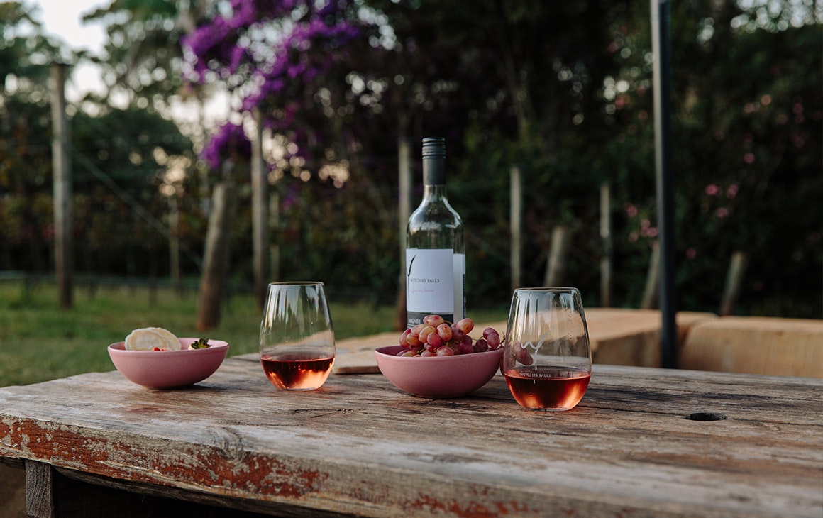 two glasses and a bottle of wine on a table in front of vineyard