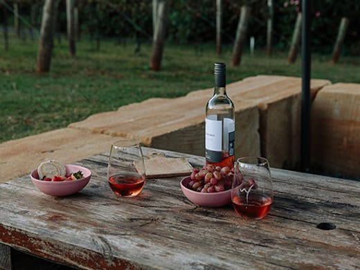 A bottle and two glasses of wine on a bench.