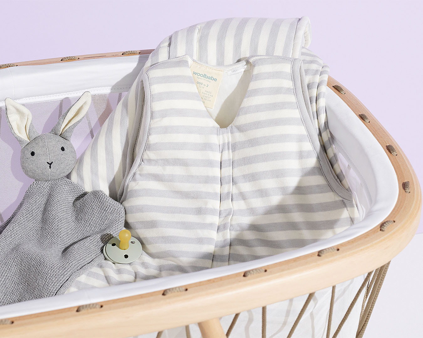 A cot with a sleeping bag babygro and stuffed bunny inside.