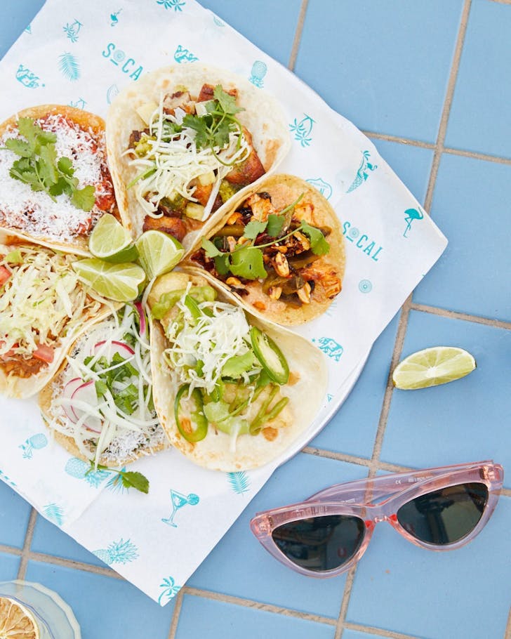 a selection of tacos laid on a socal table next to a pair on sunglasses