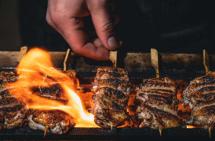 Skewered meat being cooked by the flames of habachi-style grill.