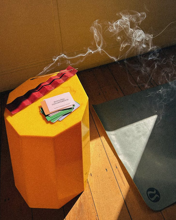 An incense burns on a bright yellow table in a warm yoga studio.