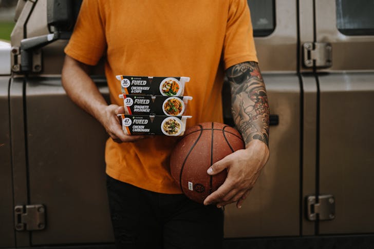 A person holding a basket ball and some Youfoodz ready made meal packs