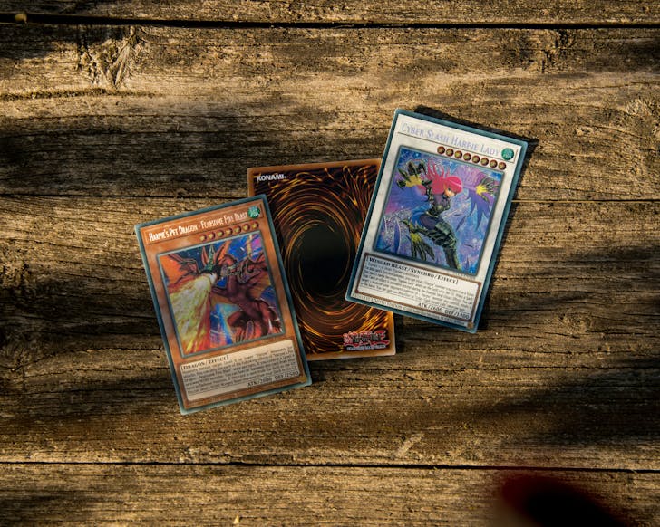 Three Yu-Gi-Oh! cards laid on an outdoor wooden table in the sunlight.