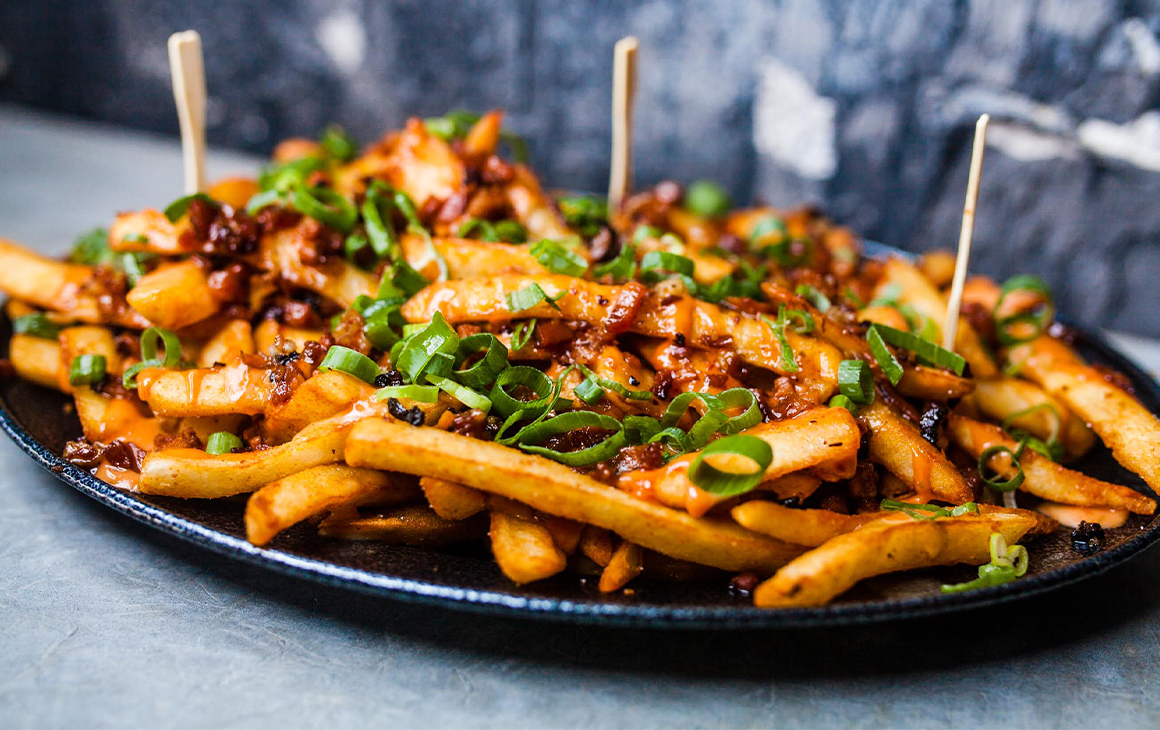 A plate of fries topped with bacon and spring onions 