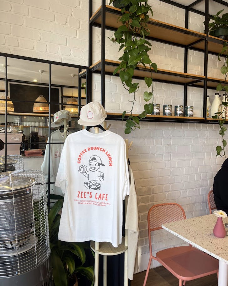 A mid-shot of inside Zee's cafe where a Zee cafe merchandise shirt is hanging up next to the dine-in seating. The colours of the interior cafe are bright and sunlit.