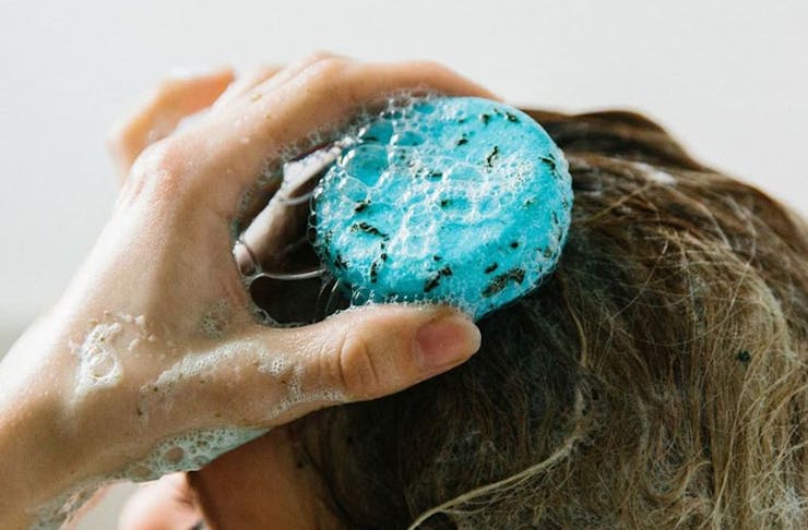 A woman washing her hair with a blue shampoo bar