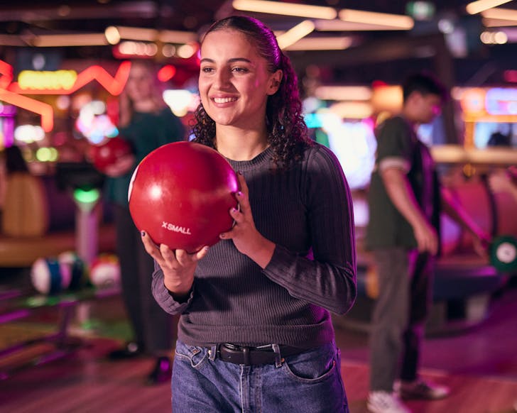 Someone holds a red bowling ball, ready to bowl.