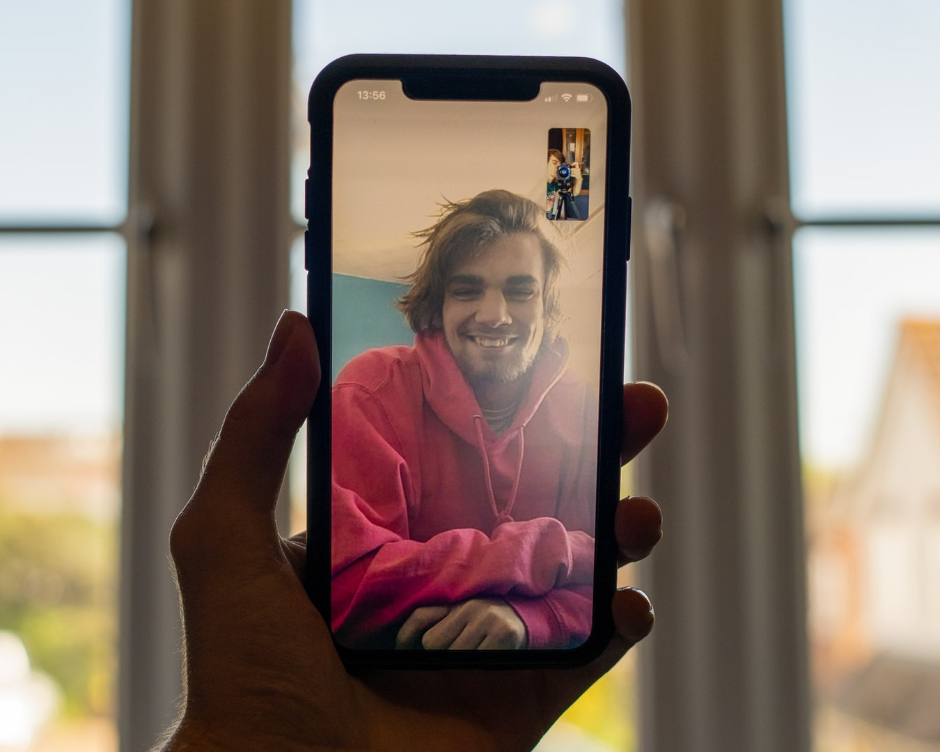 Person holding smart phone with a smiling friend on video call