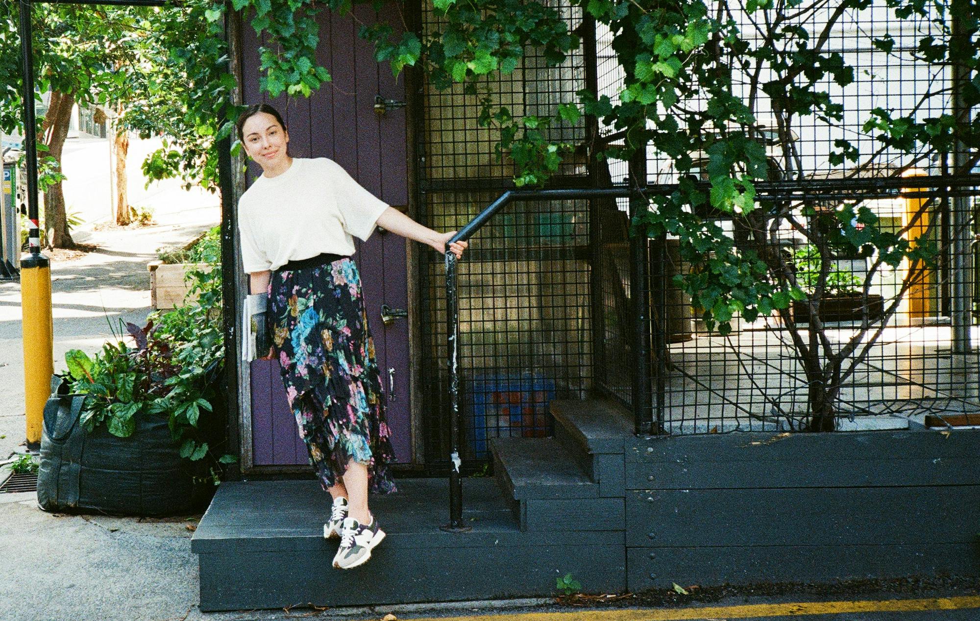 A person on a short flight of stairs, outdoors, leaning to the side but supporting their weight by holding onto the handrail. 