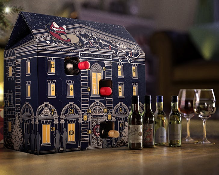 Laithwaites Wine advent calendar in the share of a small house with wine bottles on the table in front of it. 