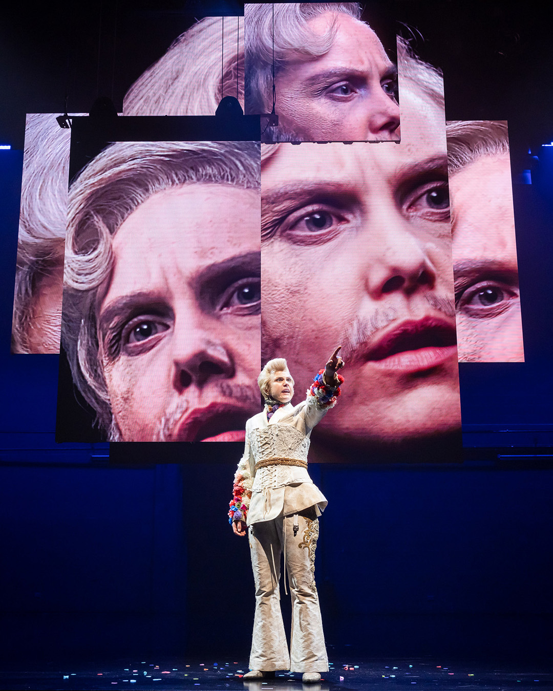 Eryn Jean Norvill on stage for The Picture of Dorian Gray, multiple video screens hang behind them with different angles of their face. 