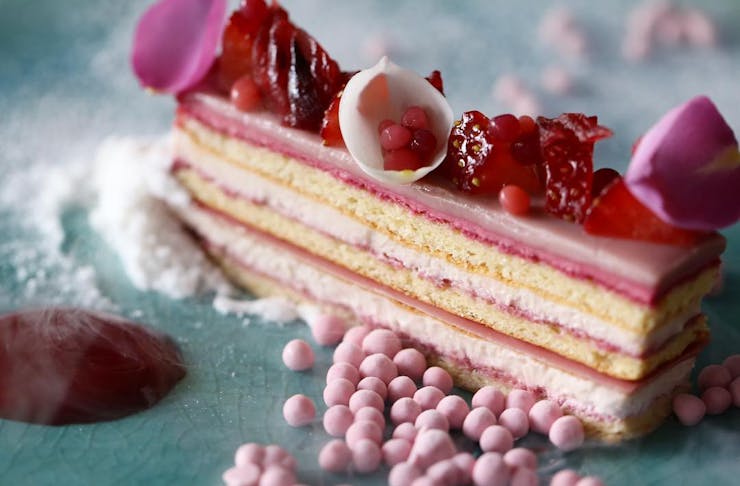 Gourmet cake-like dessert with lots of pink layers and pink fruit on top. 
