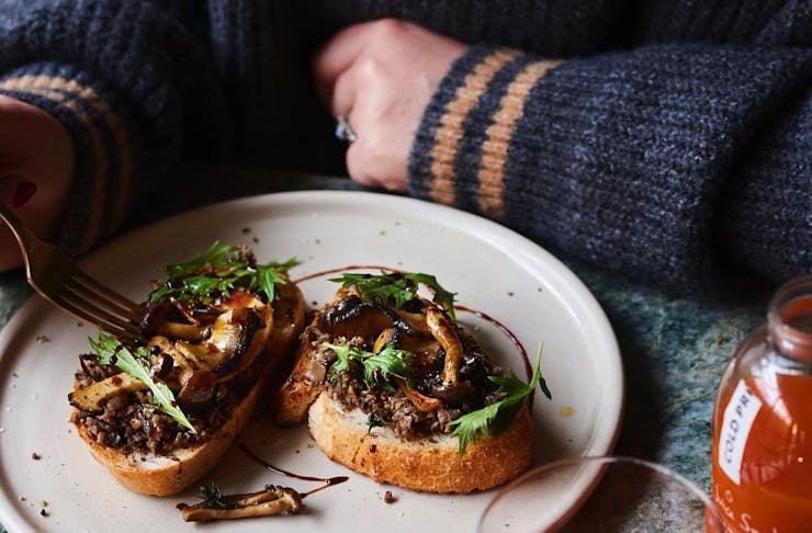 A plate with mushrooms on toast and a hand holding a fork, for national mushroom day
