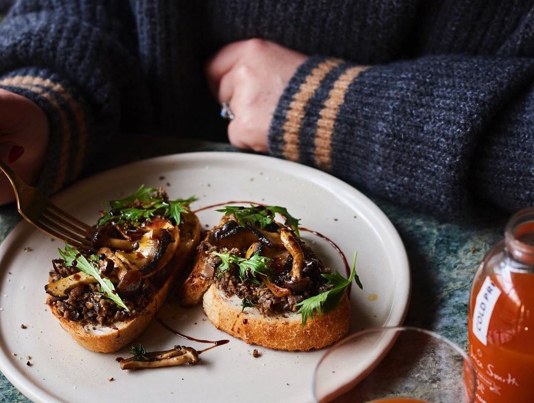 A plate with mushrooms on toast and a hand holding a fork, for national mushroom day