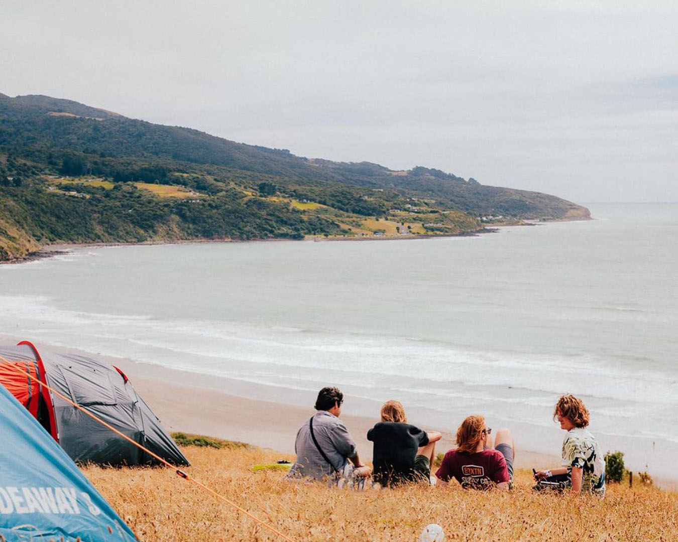 Tents in the foreground, people reclining on a sand dune and the ocean in the background atSoundsplash festival 