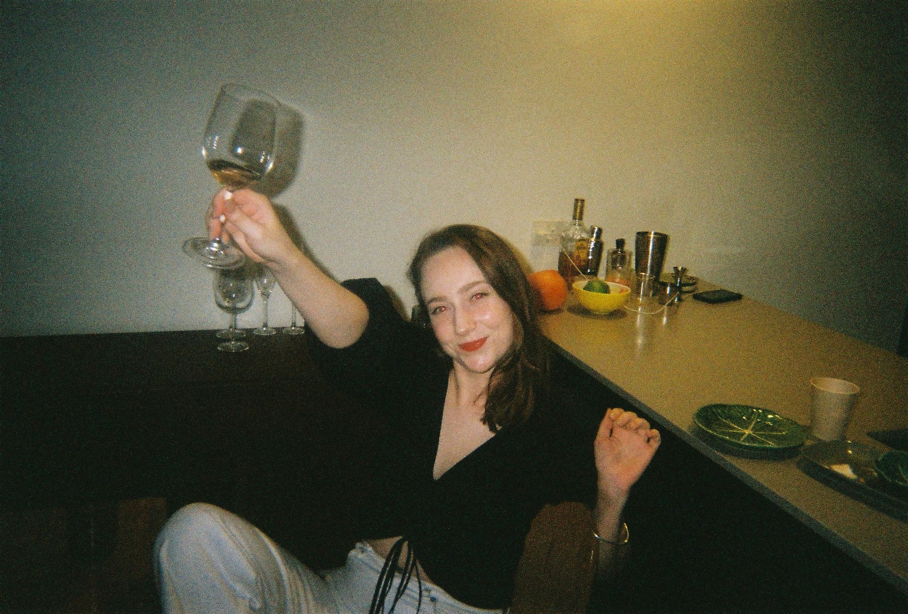 A person in the kitchen joyously holding up a wine glass with a small amount of wine in it. 